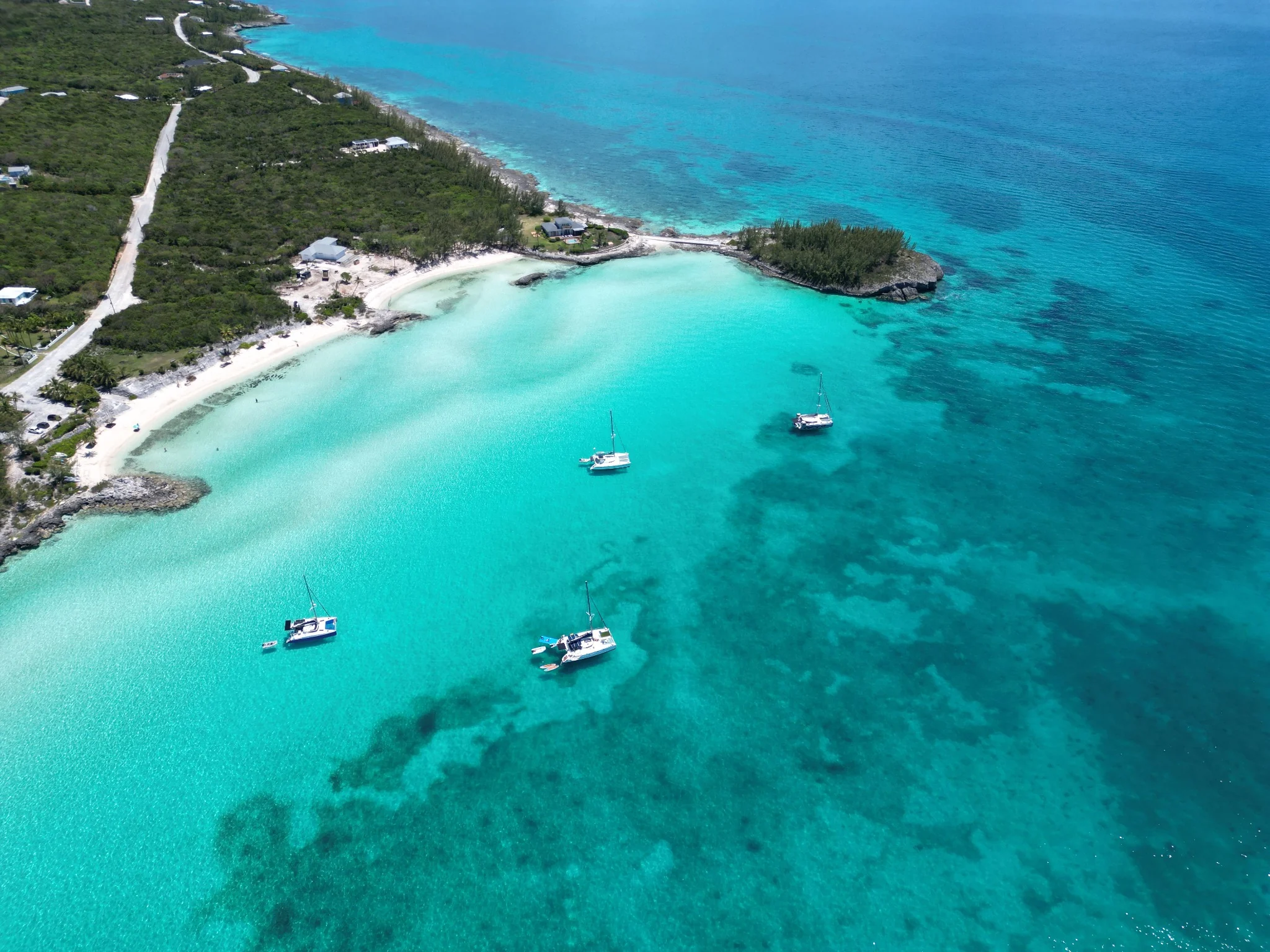 Sailboats at anchor in the turquoise water of Rainbow Bay, Eleuthera, beside a sandy shore.